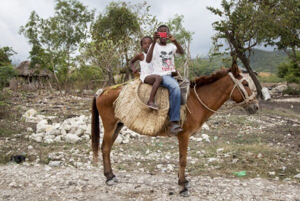 Two children sit atop a donkey taking a photo of the photographer